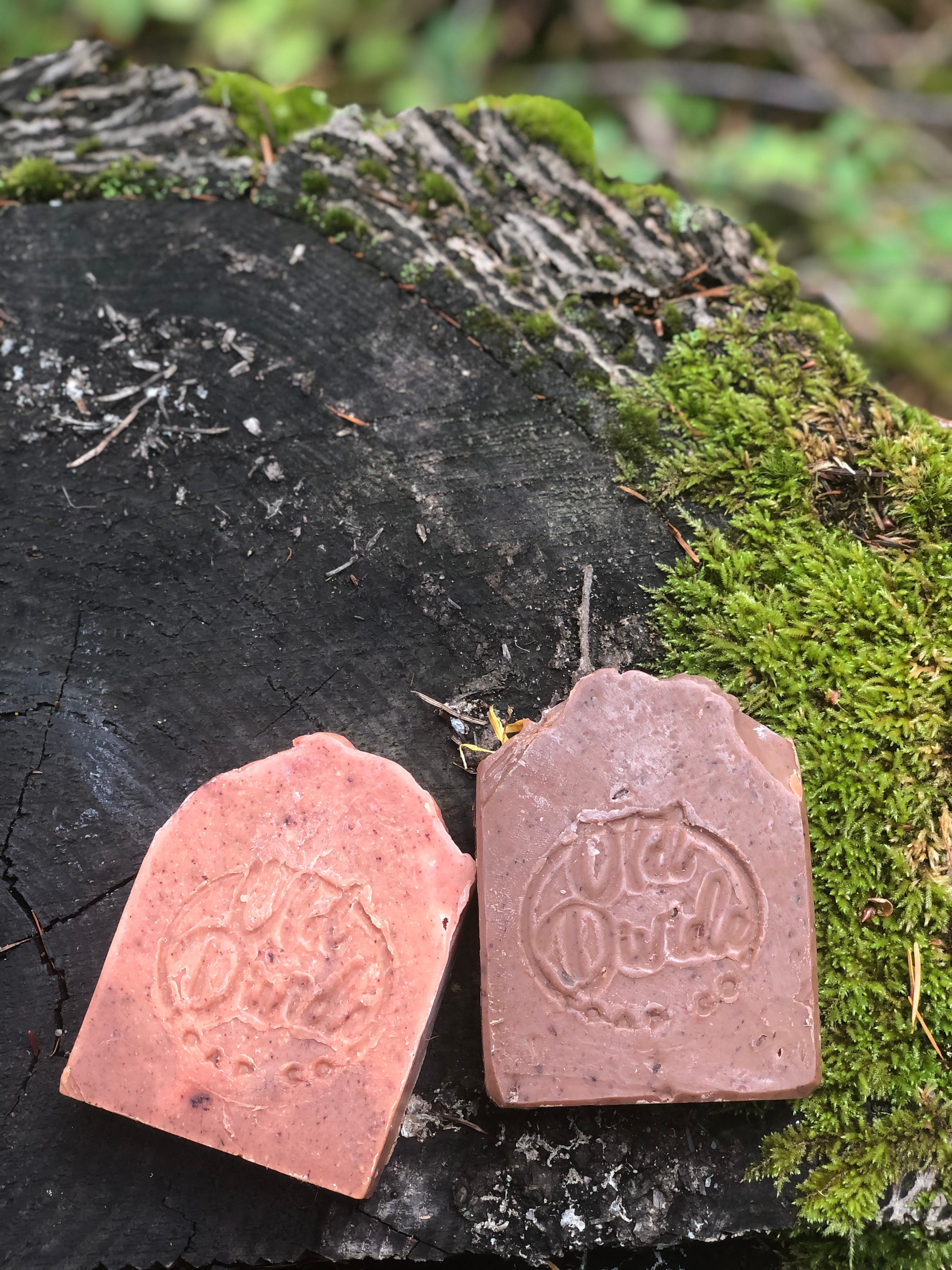 Naturally coloured earthy soap bars  in mauve and pinkish red made from essential oils, in a natural environment, on a piece of wood with moss.